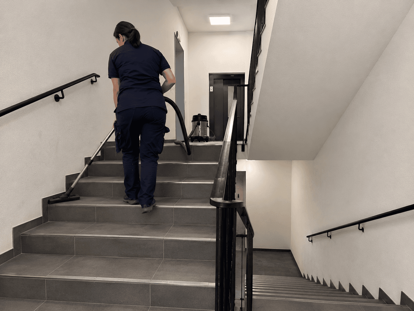 Mitarbeiterin geht mit Staubsauger die Treppe hoch