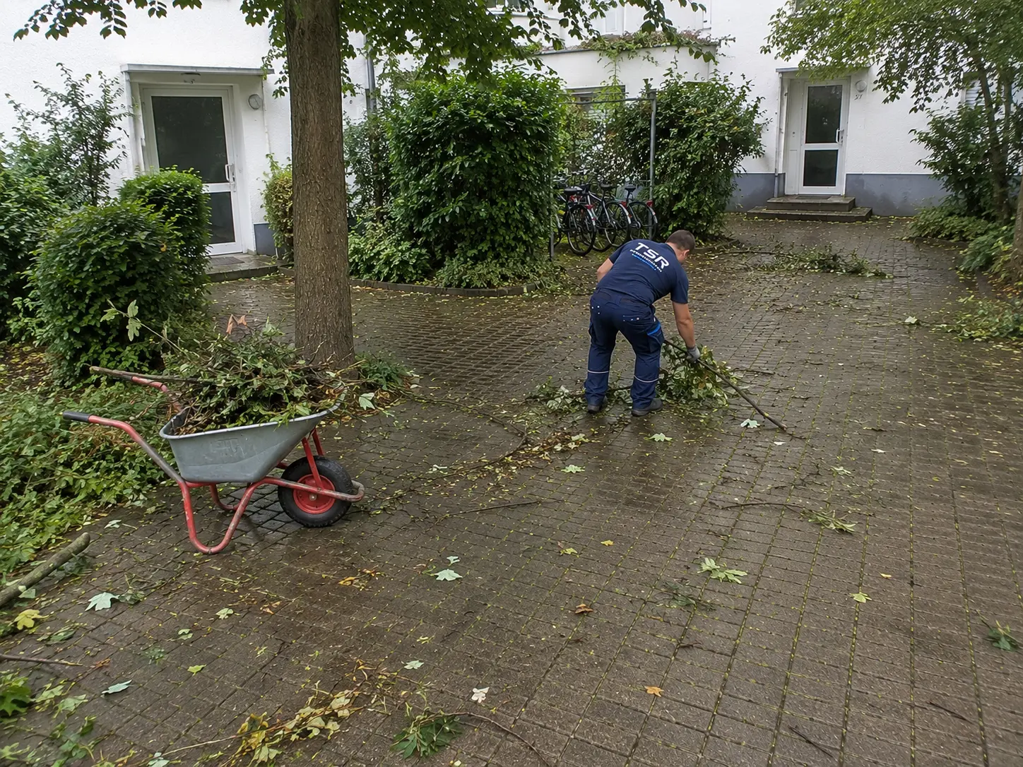 Mitarbeiter beseitigt Sturmschäden in der Grünanlage einer Wohnanlage